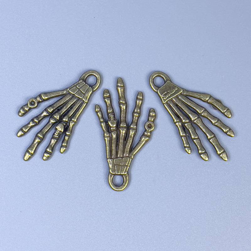 Přívěšek ve tvaru ruky kostry, bronzová barva, rozměry 35×19×2 mm ± otvor Ø 3 mm ± balení 20 g (~9 ks)
