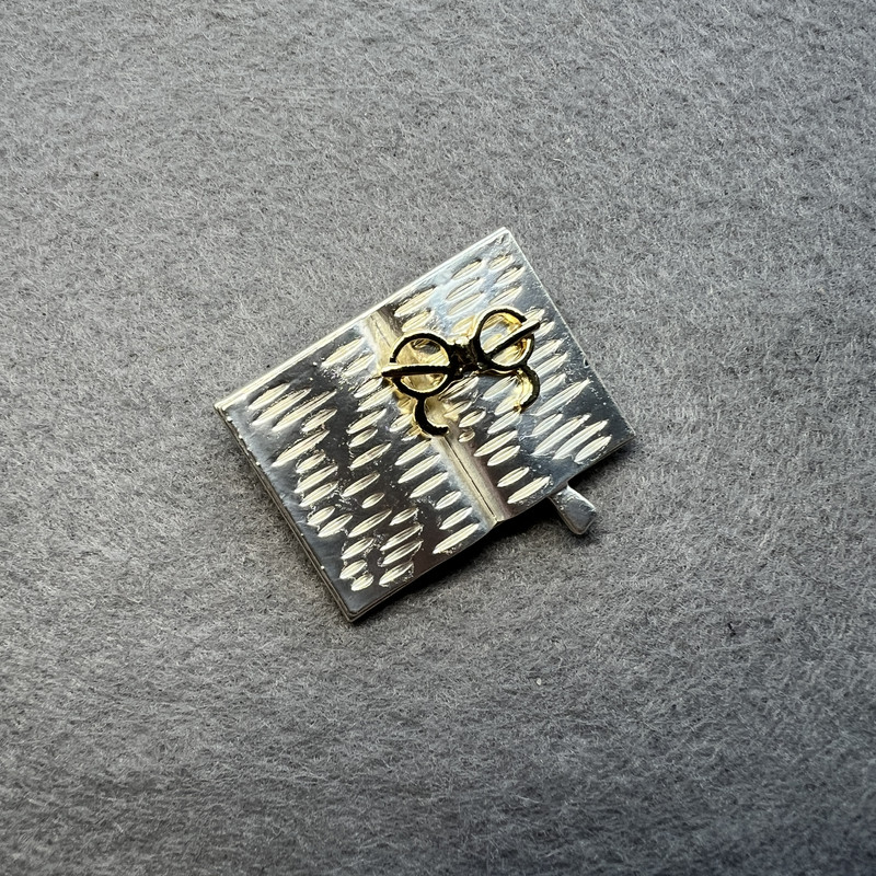 Brož 'Kniha s brýlemi', světle šedý smalt a zlatavý odstín, stříbrný kov 35×26 mm